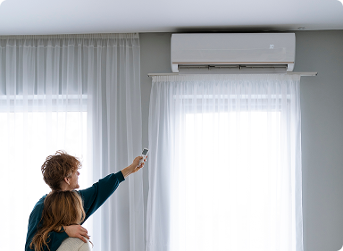 Couple using a remote to turn on their ductless air conditioner unit in a bright living room.