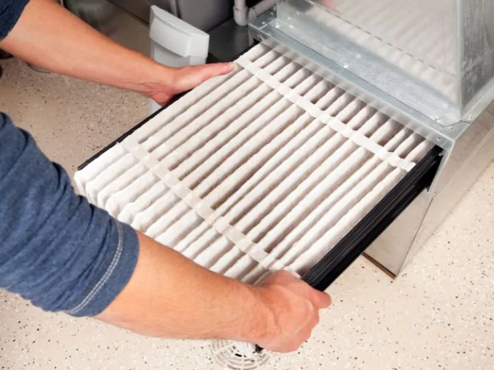 Overhead view of a person's hands sliding a clean air filter into the slot of a furnace.