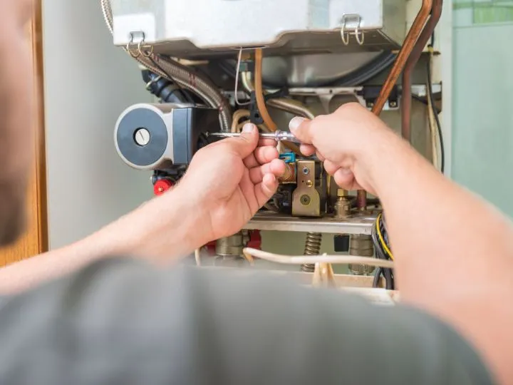 Close-up of hands changing or inspecting wires in a heating unit.