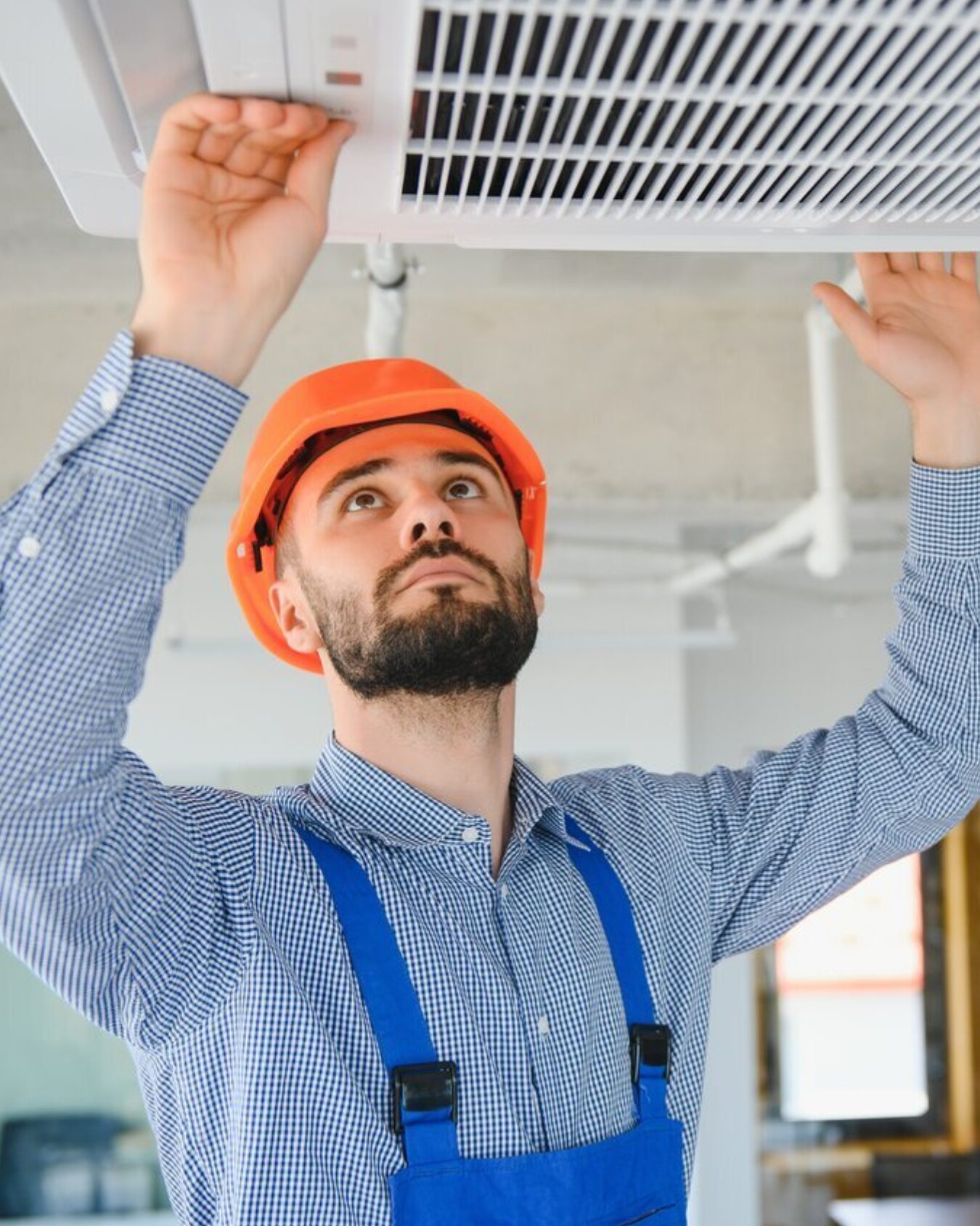 HVAC technician wearing orange construction hat inspecting a cooling unit on the ceiling of a home.