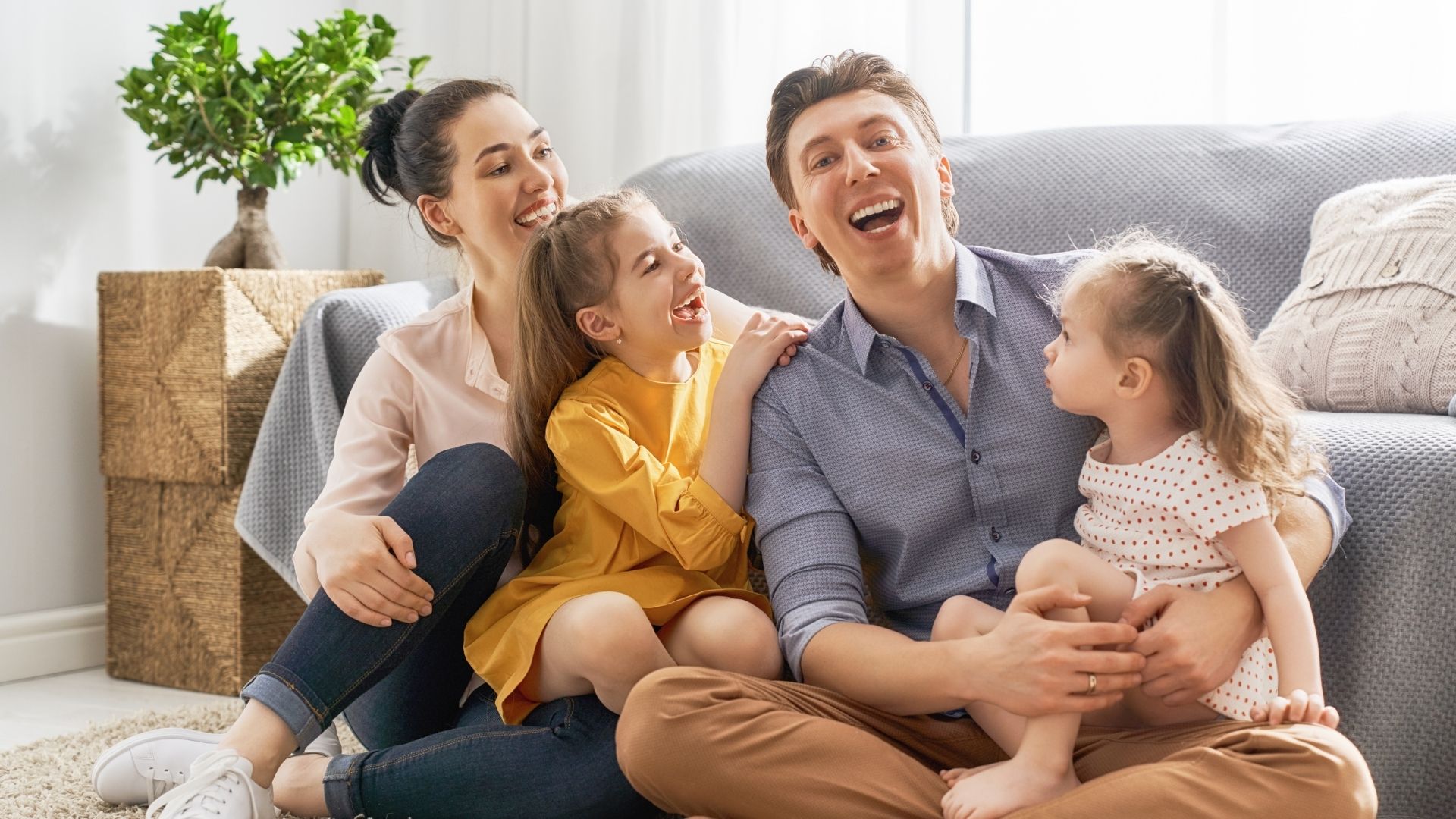 Smiling parents spending time with their two young daughters in their living room.