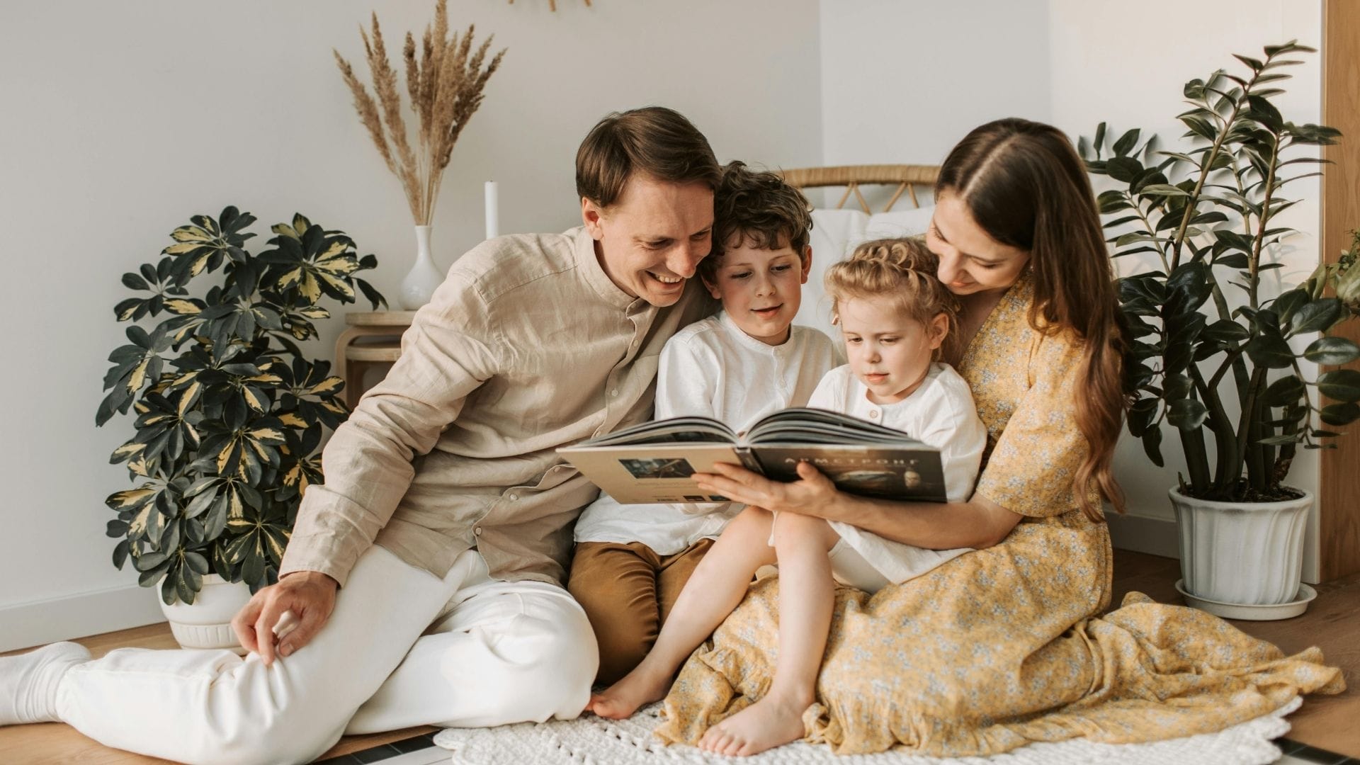 Mother and father reading a book with their 2 childern in the living room.
