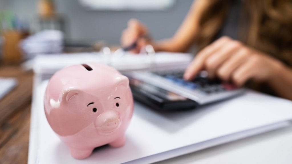 Zoom in of hand using calculator, along with documents and piggy bank on their desk