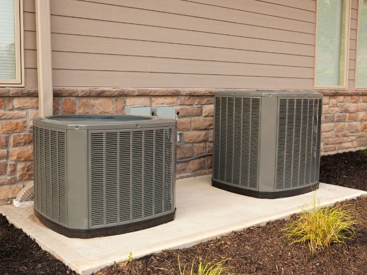 2 air conditioner units standing next to each other outside a home.
