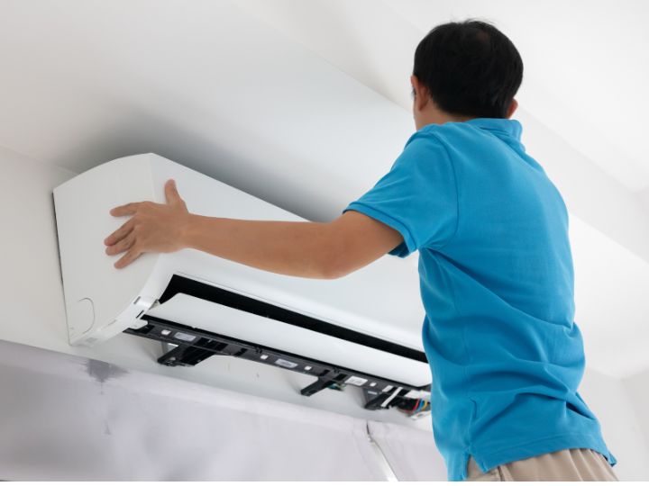 Man installing a ductless air conditioning system on the top of a wall under the ceiling.