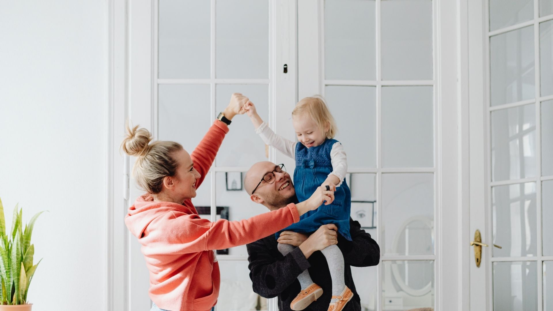 A smiling family with parents and a small girl in the living room.
