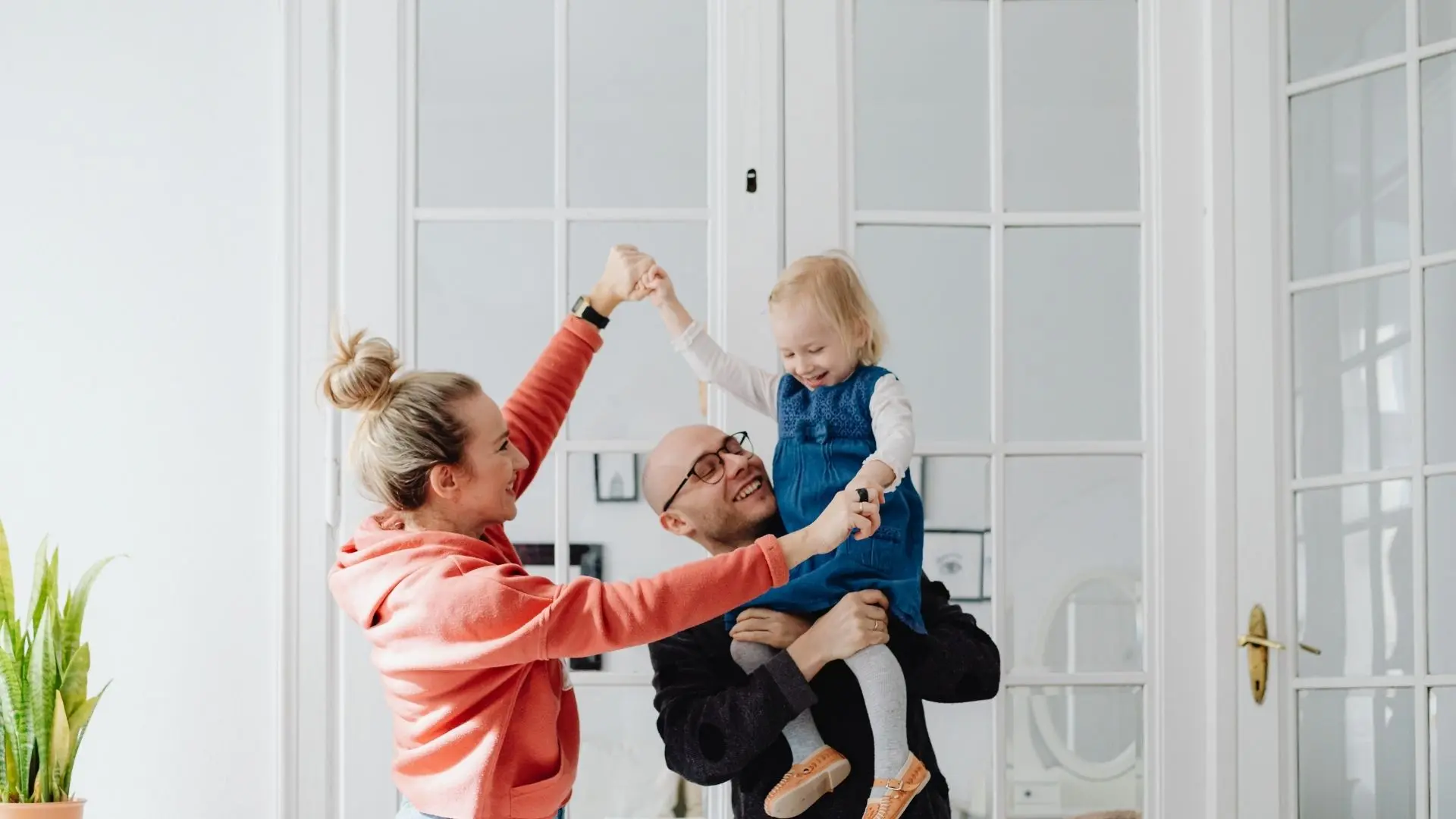A smiling family with parents and a small girl in the living room.