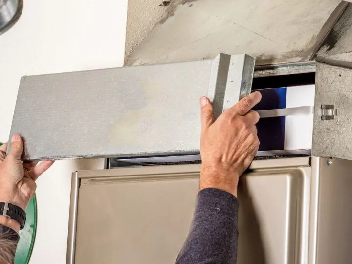 Close-up of hands moving panel off of a furnace unit.