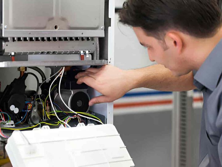 An HVAC technician inspecting and adjusting mechanical components and wiring of a heating system.