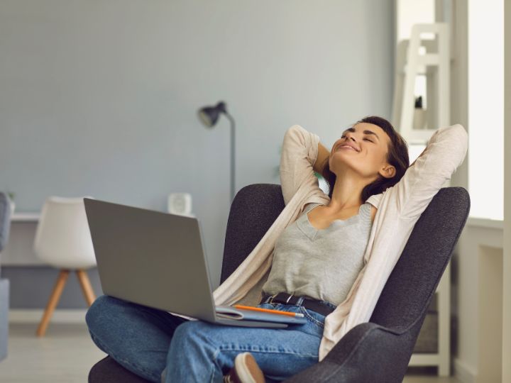Woman relaxing in chair with her hands behind her head with a laptop on her lap.