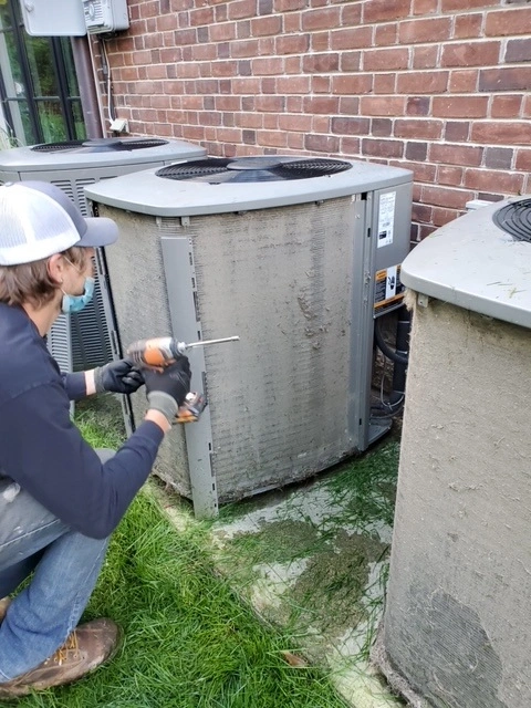 Joe's Heating and Air Conditioning HVAC technician inspecting an AC unit outside a home.