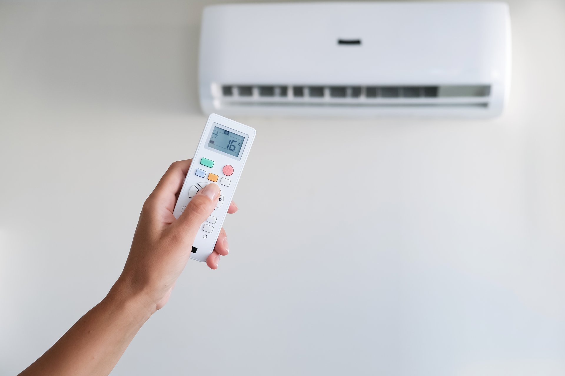 A hand with a remote control adjusting air conditioner temperature inside home.